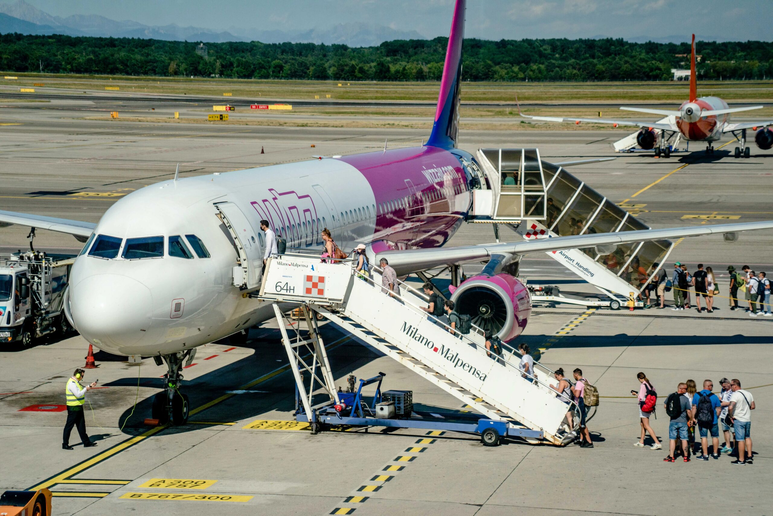 long-term dog boarding for frequent travelers - Travelers board an airplane at Milan Malpensa Airport on a sunny day, showcasing modern air travel.