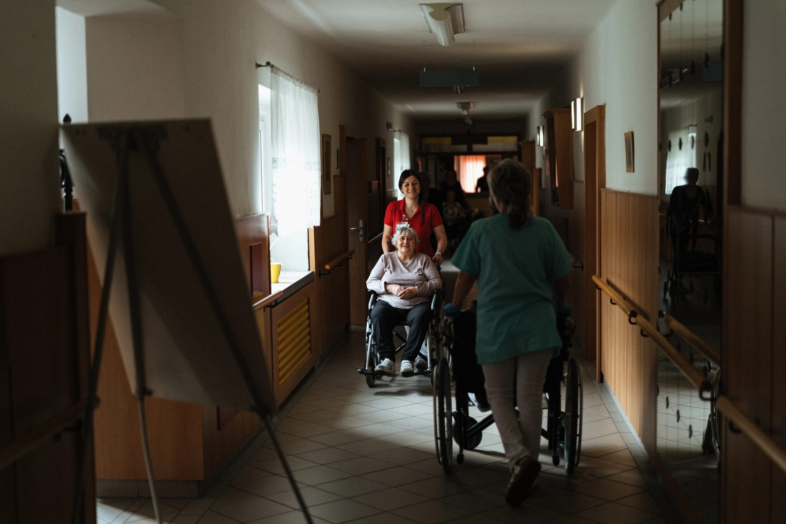 basic dog training commands every dog should know - Caregiver assisting elderly woman in a wheelchair through a retirement home corridor.