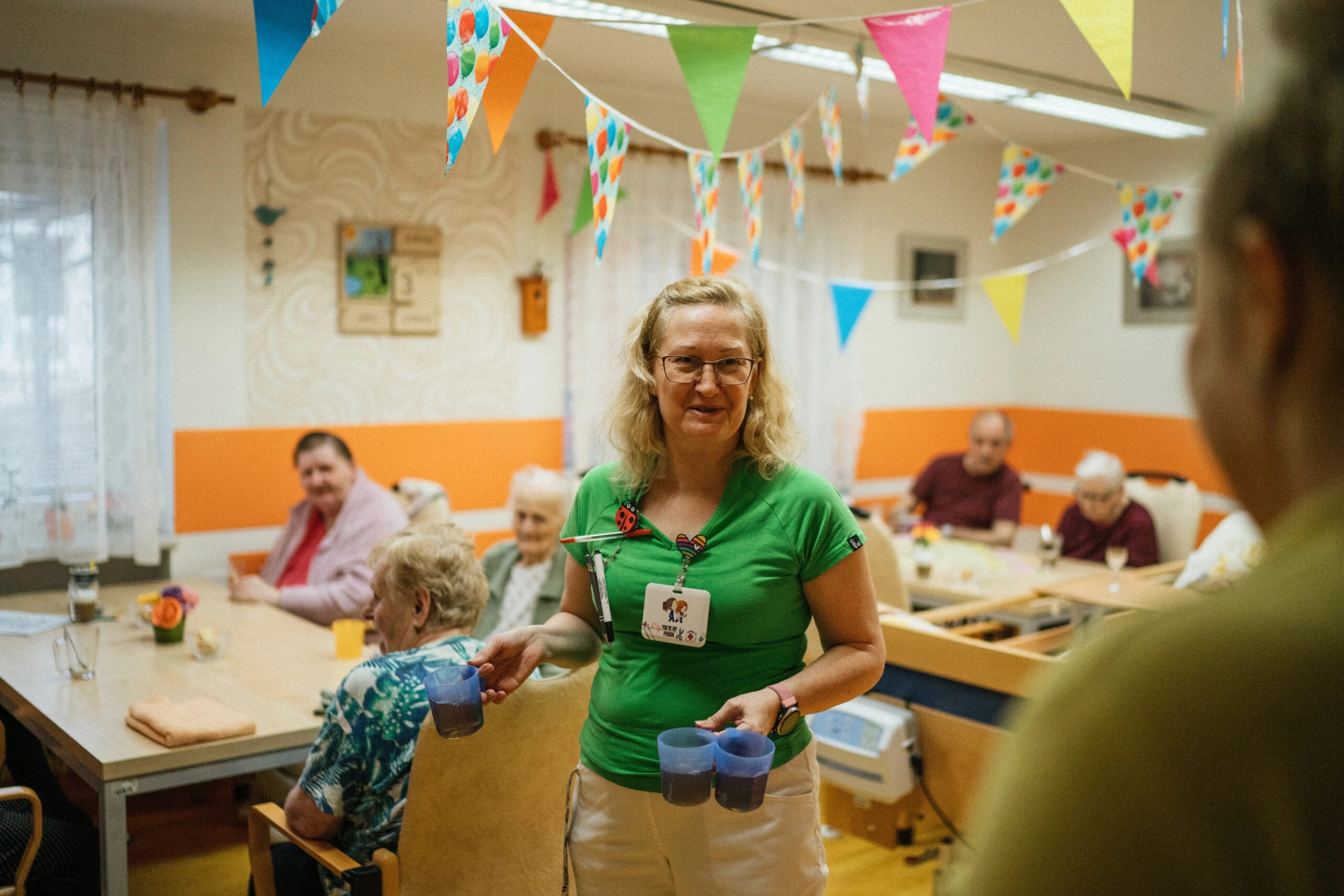 dog separation anxiety solutions for working professionals - A caregiver serving drinks to elderly residents in a cheerful nursing home setting.