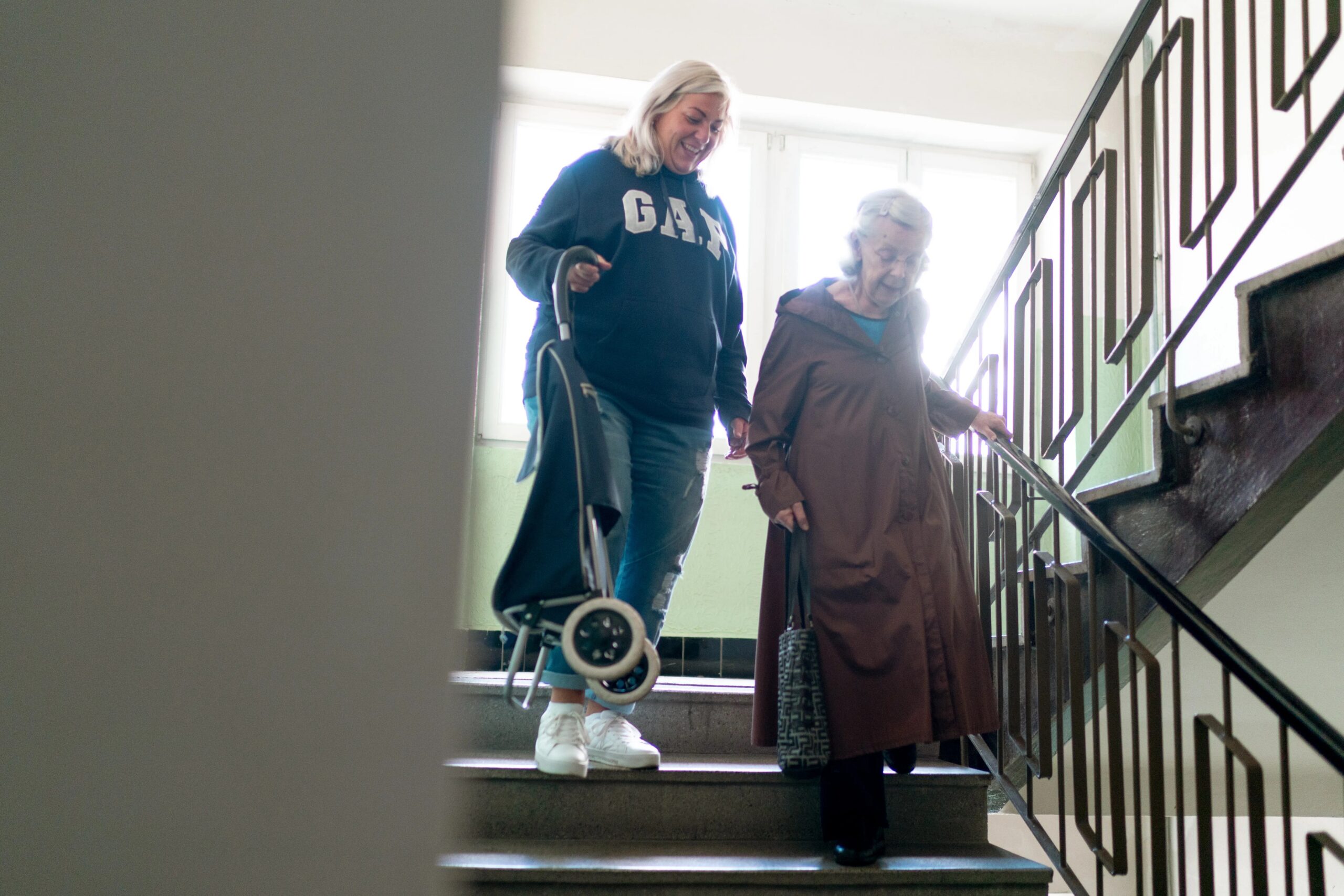 fun activities for dogs while owners are at work - Caregiver helps senior woman navigate stairs indoors, emphasizing elderly care and support.
