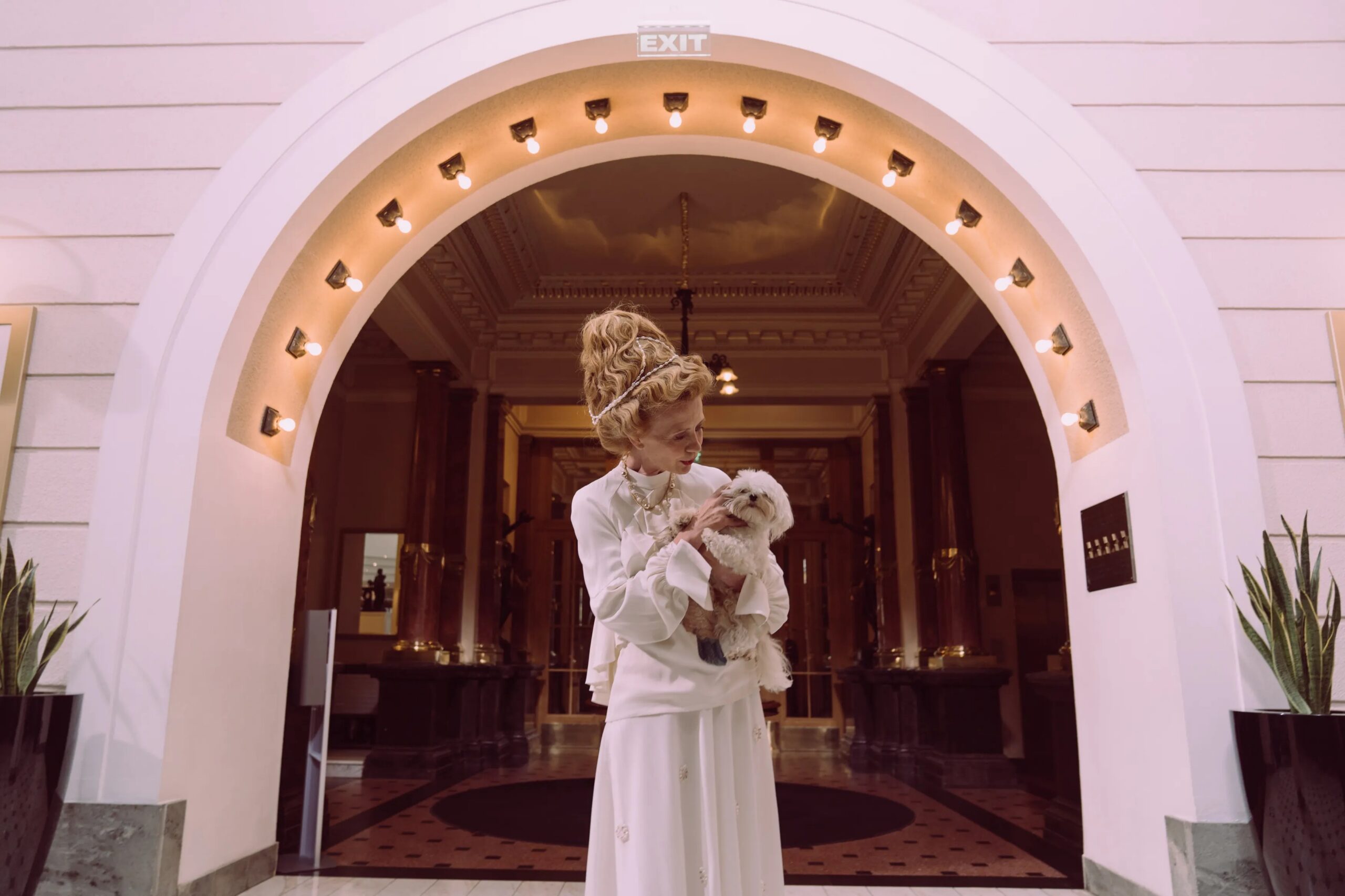 luxury dog boarding amenities The Woodlands - A senior woman elegantly dressed, holding a small dog in a luxurious hotel lobby.