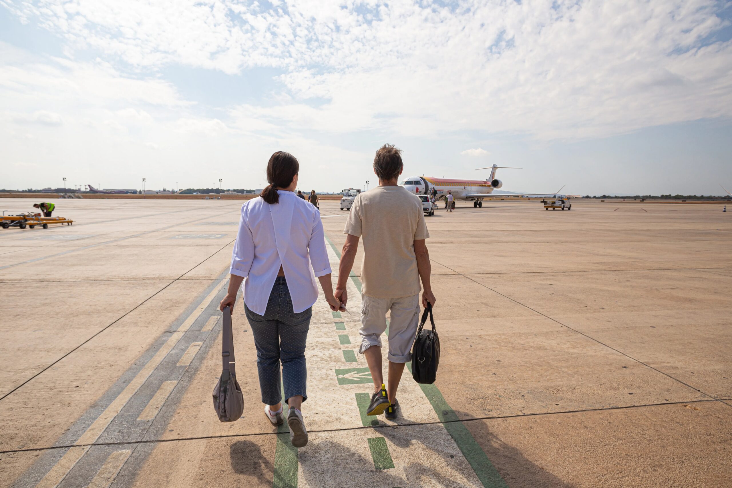 long-term dog boarding for frequent travelers - Couple holding hands, walking on the runway towards a plane at Valencia Airport in Spain.