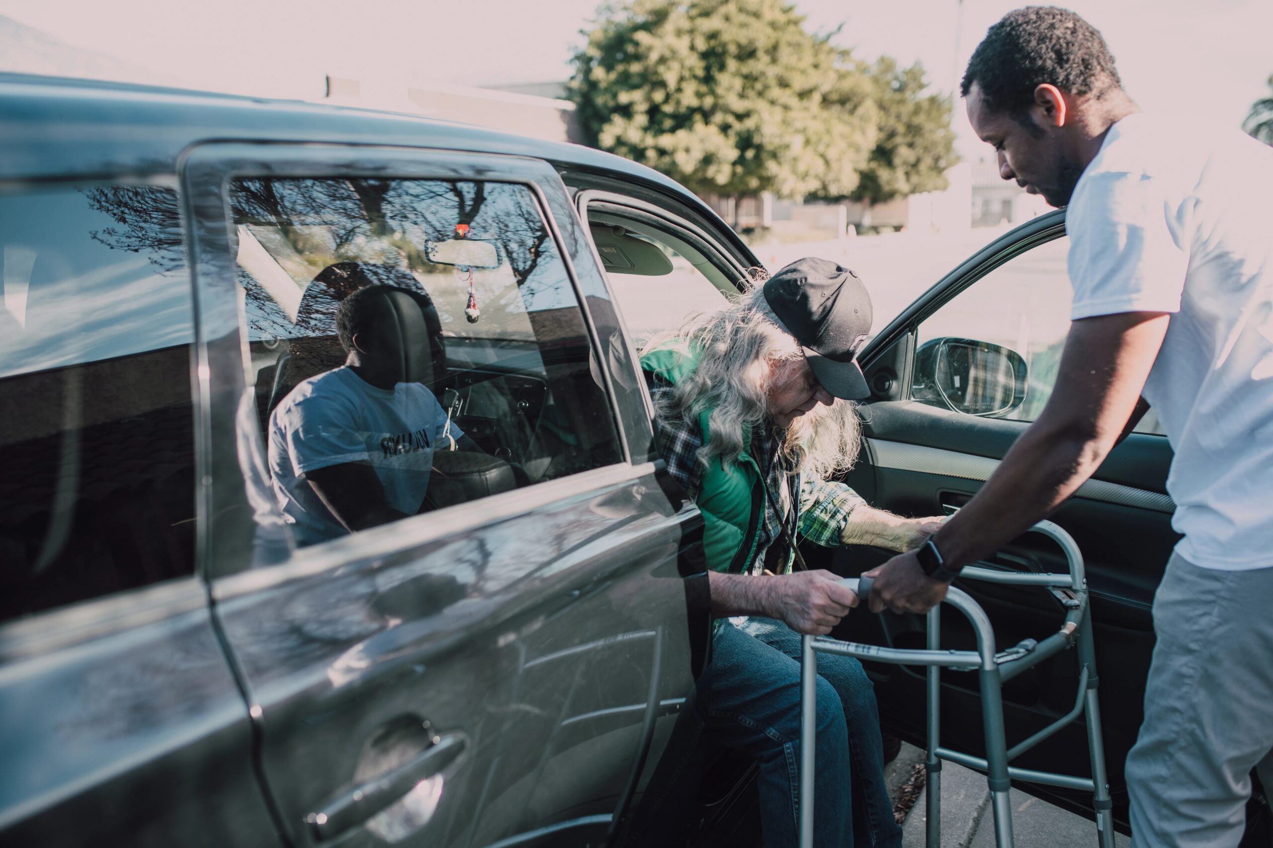 dog separation anxiety solutions for working professionals - Two men help an elderly person with a walker get out of a car outdoors.