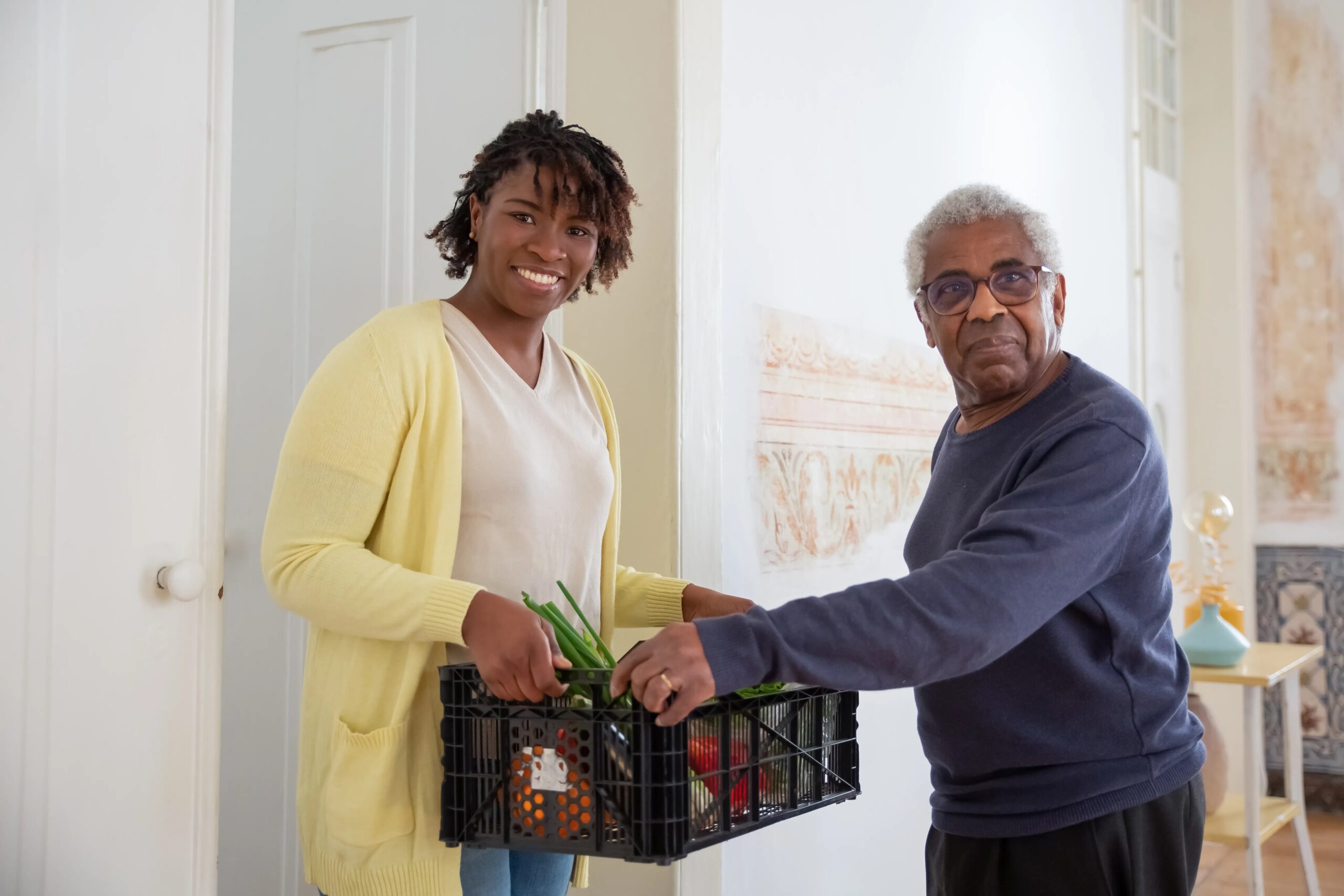 choosing the right dog daycare for your dog's temperament - Smiling woman assists a senior man with food delivery indoors, promoting community support and care.