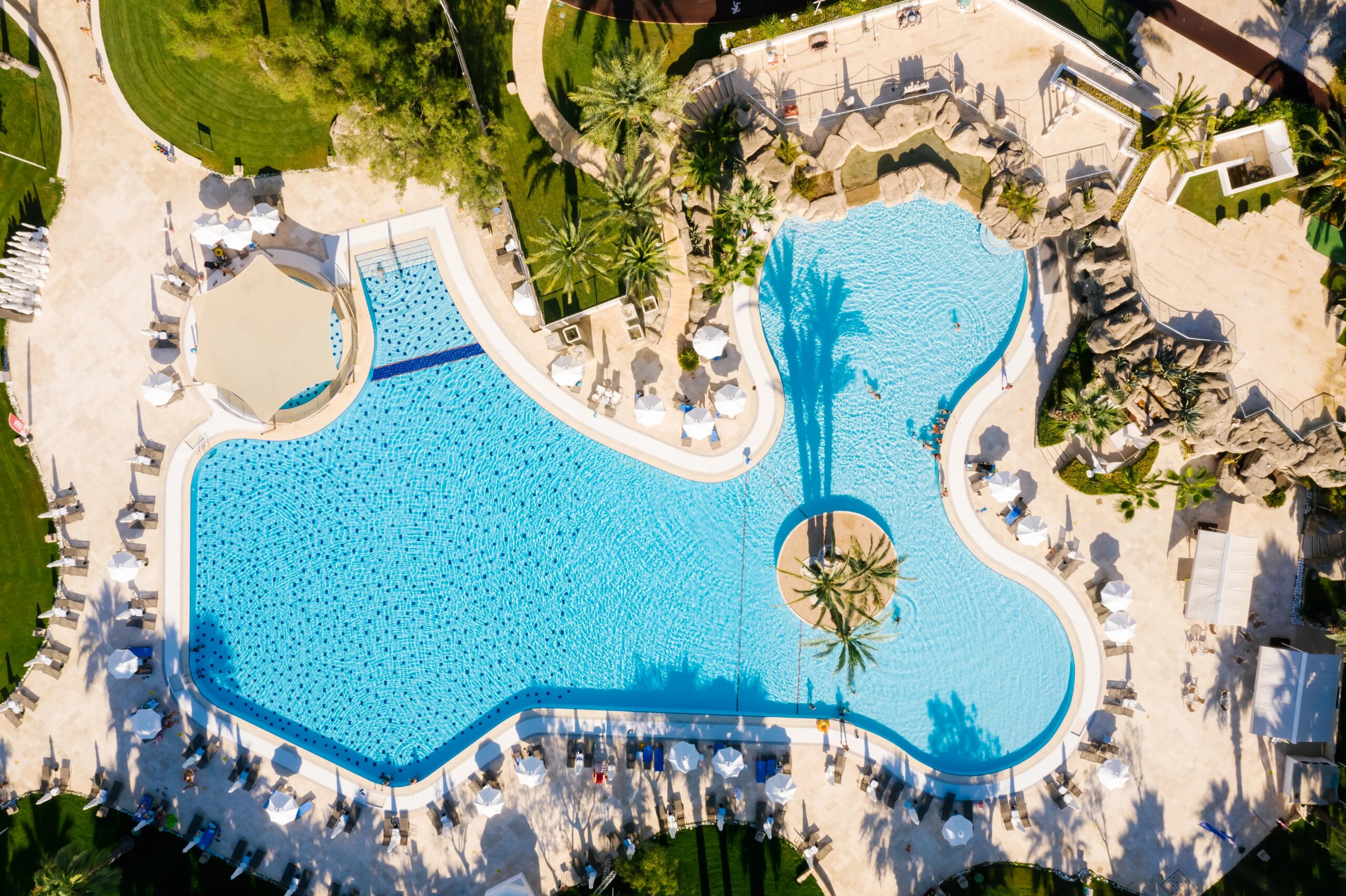 luxury dog boarding amenities The Woodlands - Stunning aerial shot of a resort swimming pool with surrounding sunbathing area and lush greenery.
